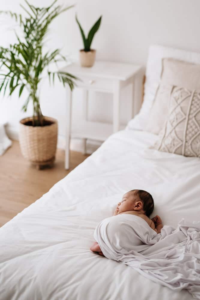 Schlafendes Baby zugedeckt mit einer weißen Decke auf dem Bett
