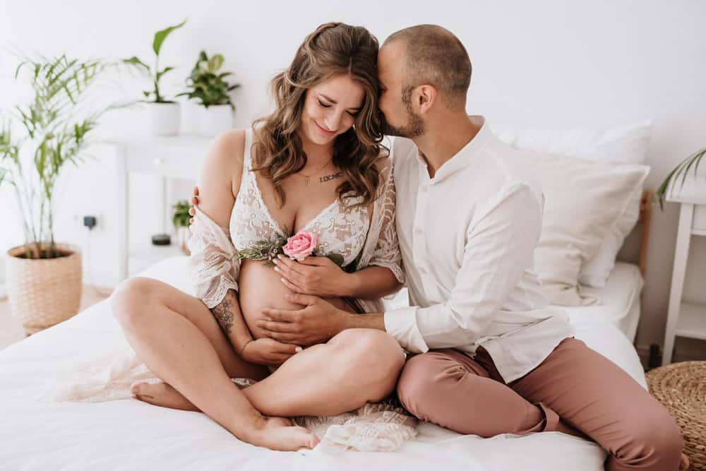 Schwangere in Dessous mit Partner auf dem Bett