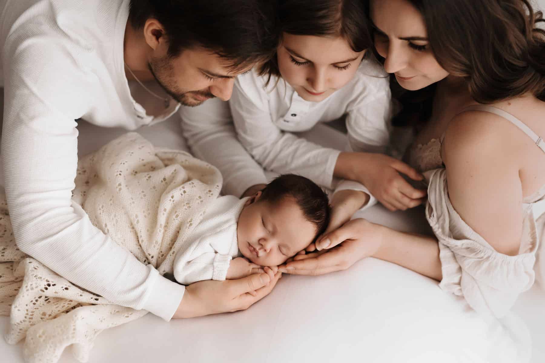 Baby liegt auf einer weißen Decke und wird von der ganzen Familie gehalten