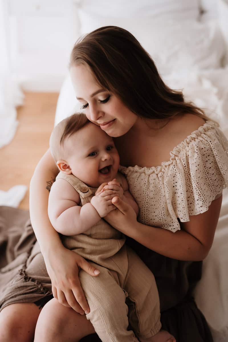 Mutter und 6 Monate Ales Kind sitzen auf dem Bett und kuscheln