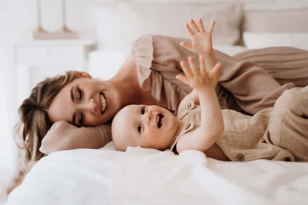 Mutter und Kleinkind liegen lachend nebeneinander auf dem Bett