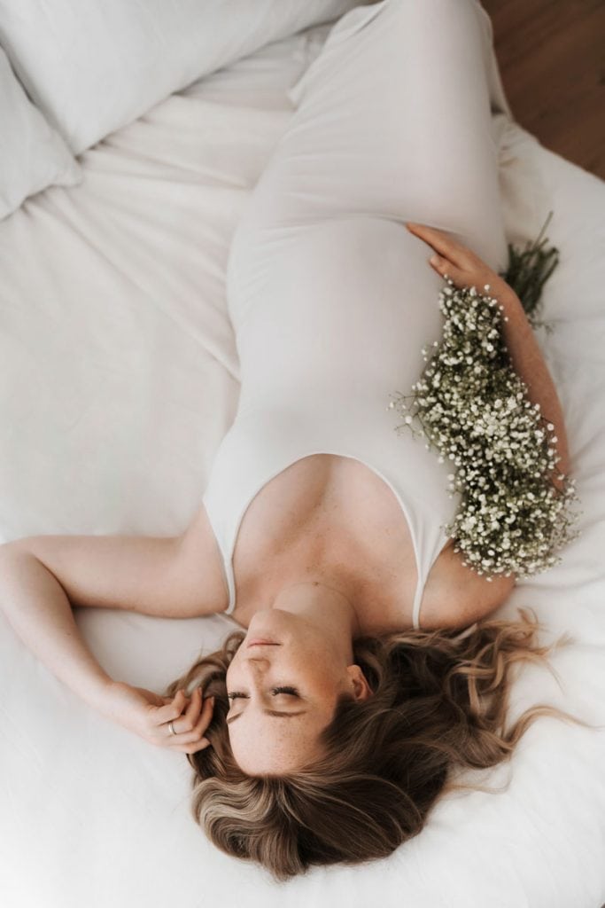 Schwangere in engem Kleid liegt auf dem Bett mit Blumen im Arm