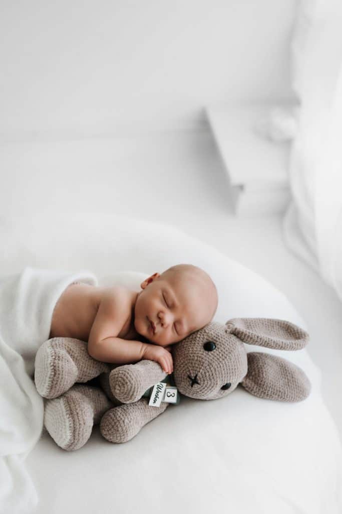 Baby kuschelt mit einem großen Hasen auf einer weißen Decke