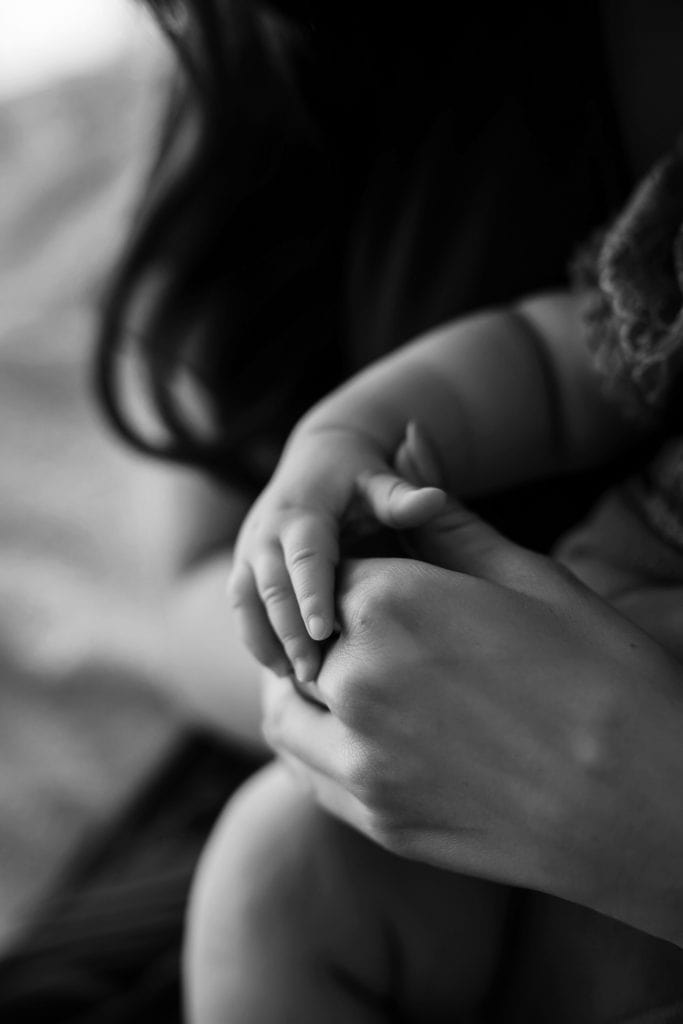 Schwarz-weiß Detailaufnahme der Hände einer Mama und ihres Babys, die sich sanft berühren. Ein intimer, liebevoller Moment voller Verbundenheit und Geborgenheit.